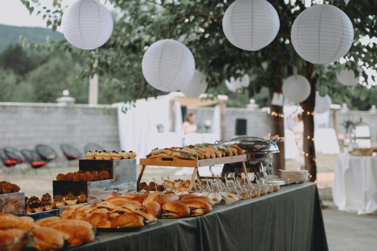 An elegant outdoor buffet featuring sandwiches and pastries under decorative lanterns.